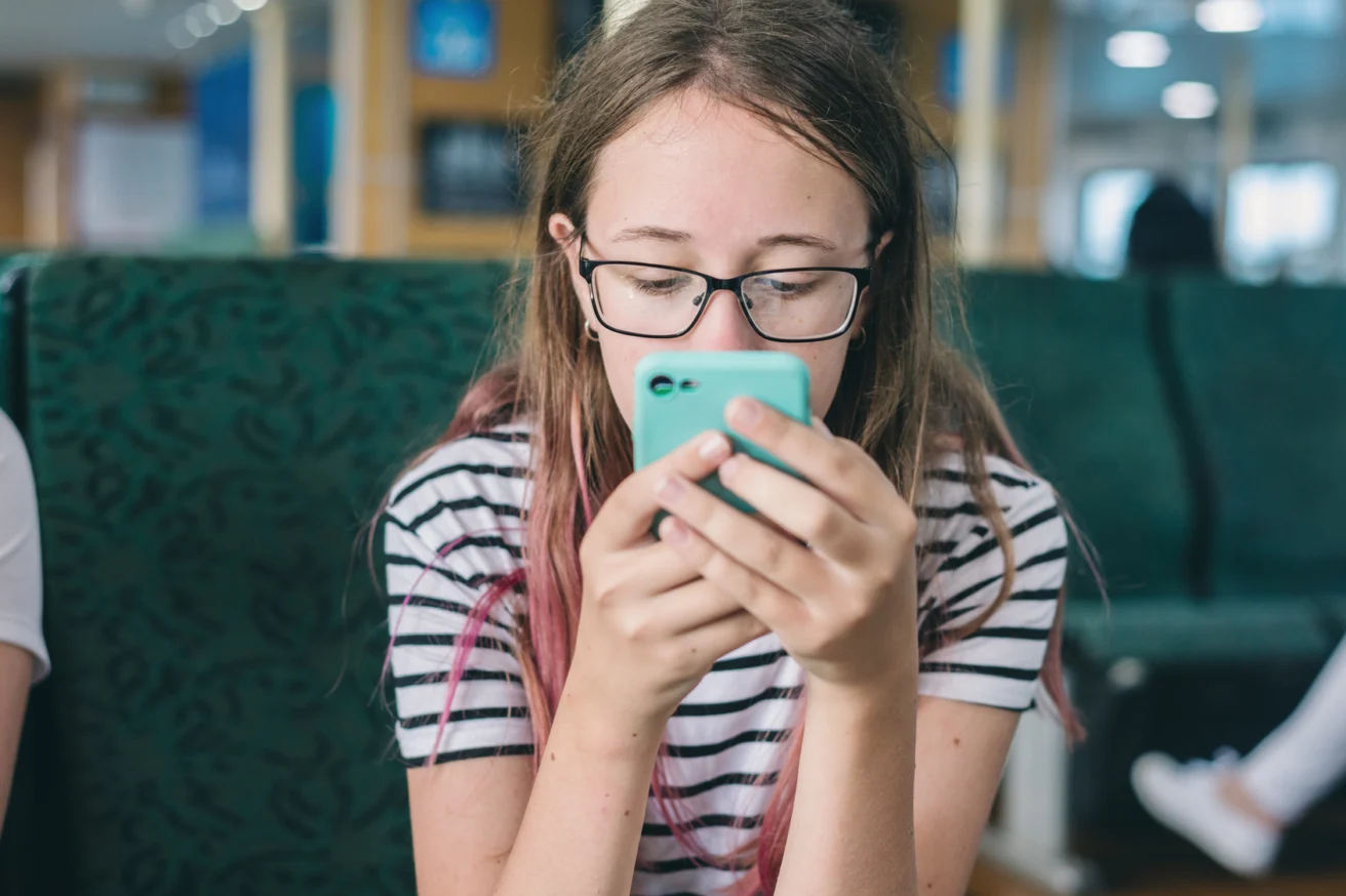 Teen staring at a glowing phone screen in a dark room, symbolizing social media addiction and isolation