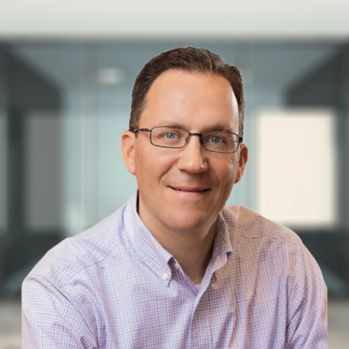 A man in a navy blazer and light-blue shirt stands smiling in a professional office environment. John Taylor, Chief Operating Officer at Postman Law.