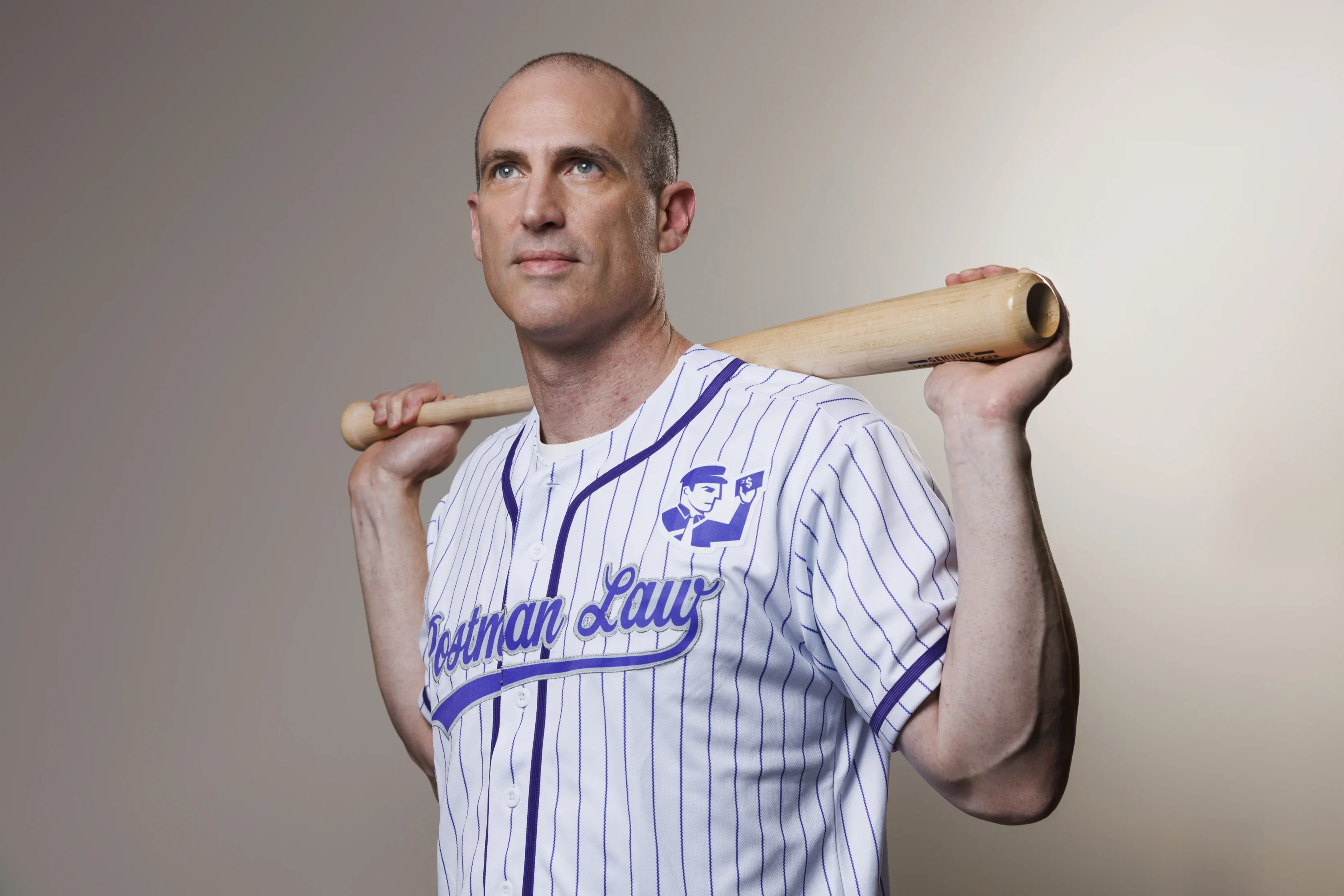 A man in a white pinstriped baseball jersey holds a bat across his shoulders, looking slightly upward against a plain background.