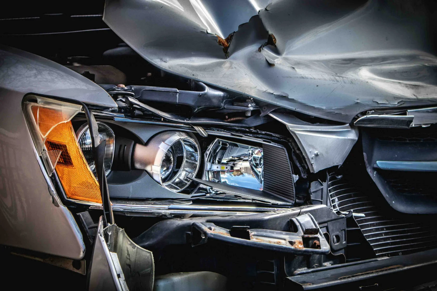 Close-up of a car with significant front-end damage, showing a crumpled hood and exposed headlight after a collision.