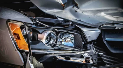Close-up of a car with significant front-end damage, showing a crumpled hood and exposed headlight after a collision.