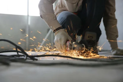 A person using an angle grinder on a metal object, producing bright sparks on the floor.
