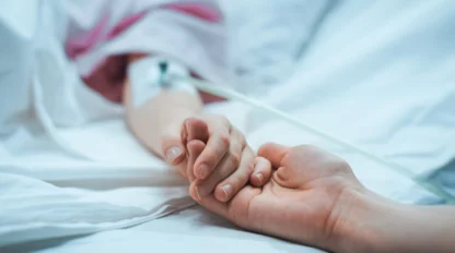 A guardian holding a patient's hand in a hospital bed.