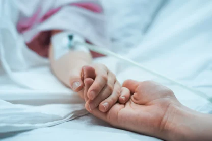 A guardian holding a patient's hand in a hospital bed.