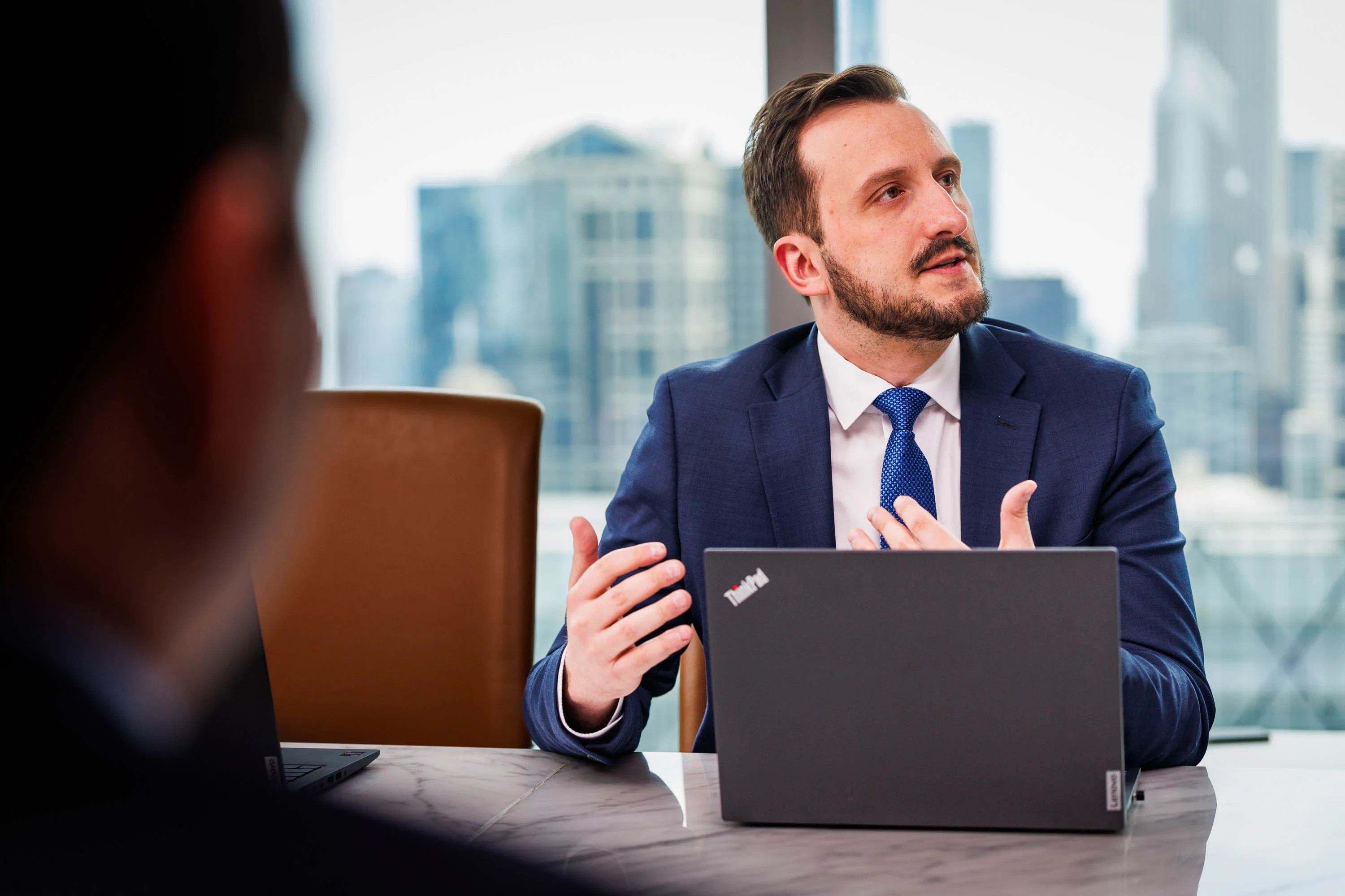 A lawyer with his laptop out in front him, speaking during a meeting.