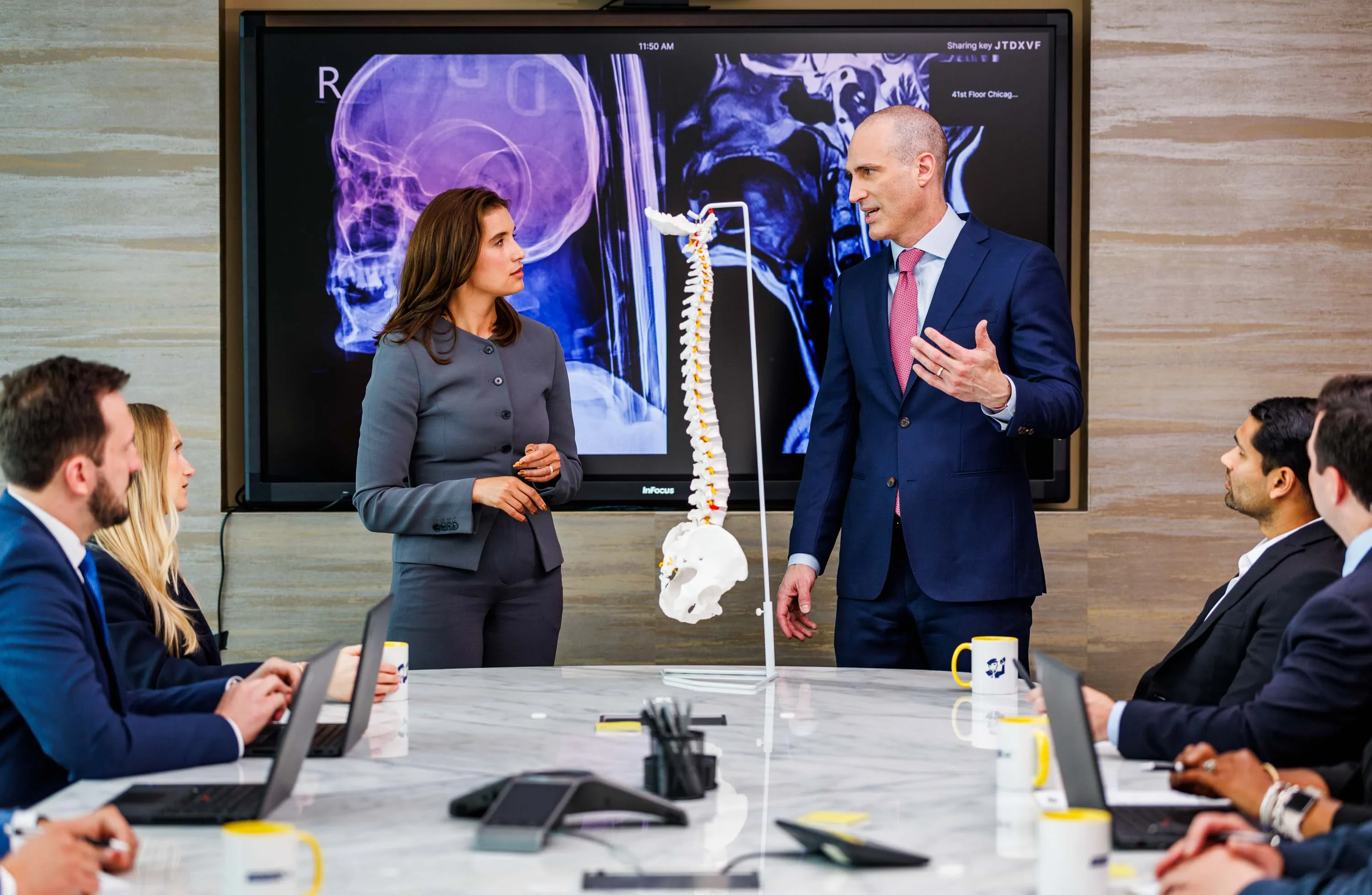 A group of lawyers in a meeting examining a model of a spine.